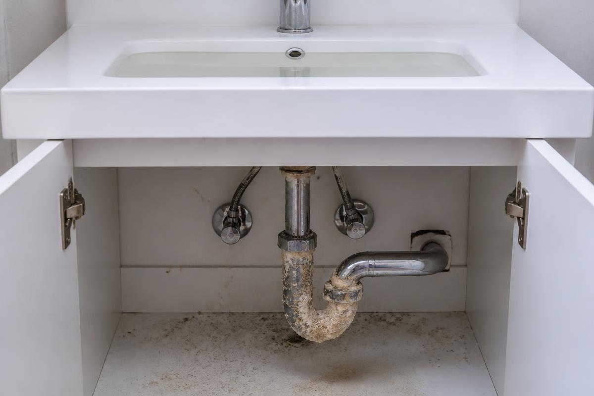 Stark verkalkter und verstopfter Siphon unter einem Waschbecken